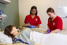 Two nursing students work on a medical training mannequin.